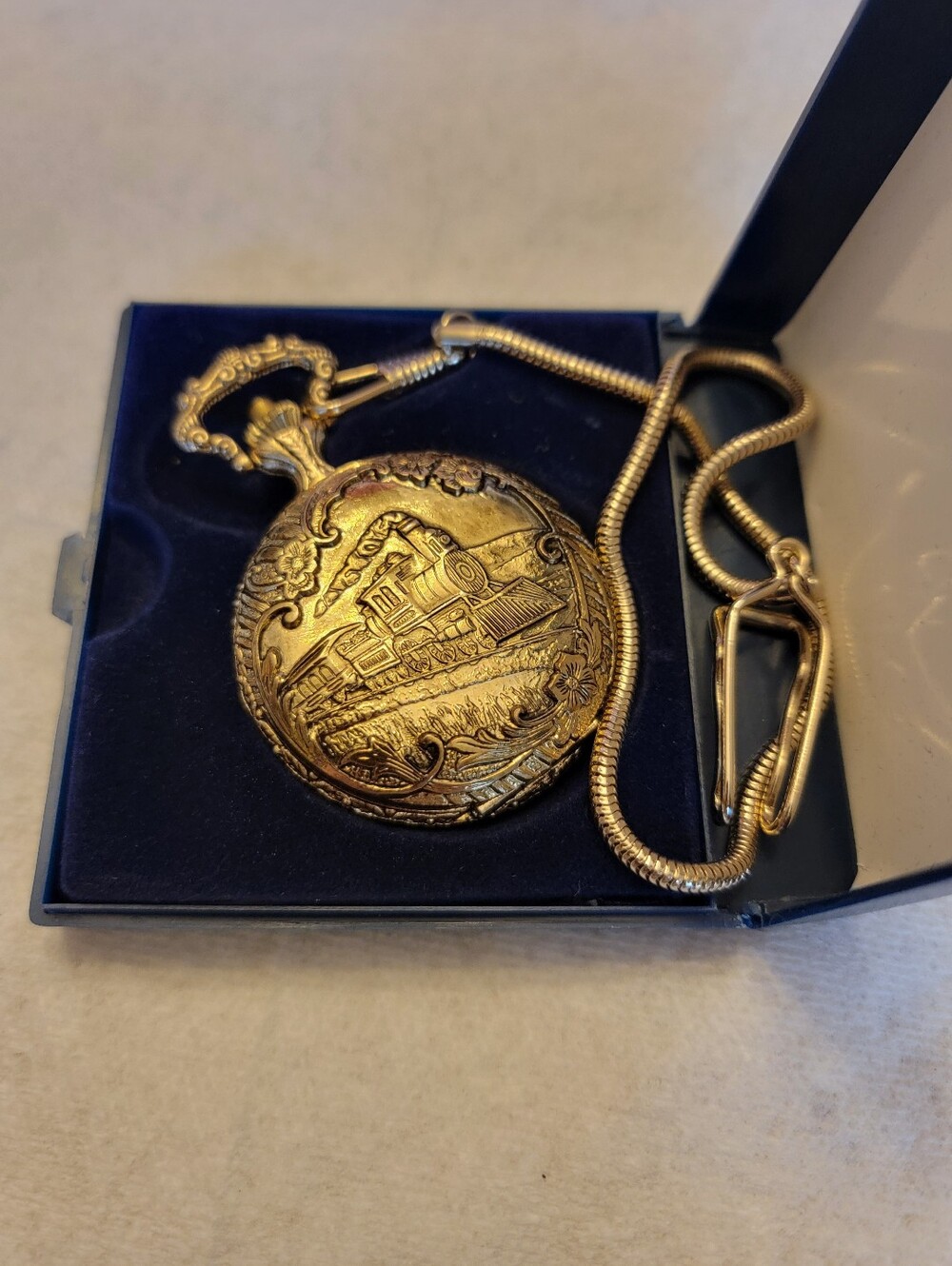 Vintage gold-tone pocket watch has a raised steam engine train motif.